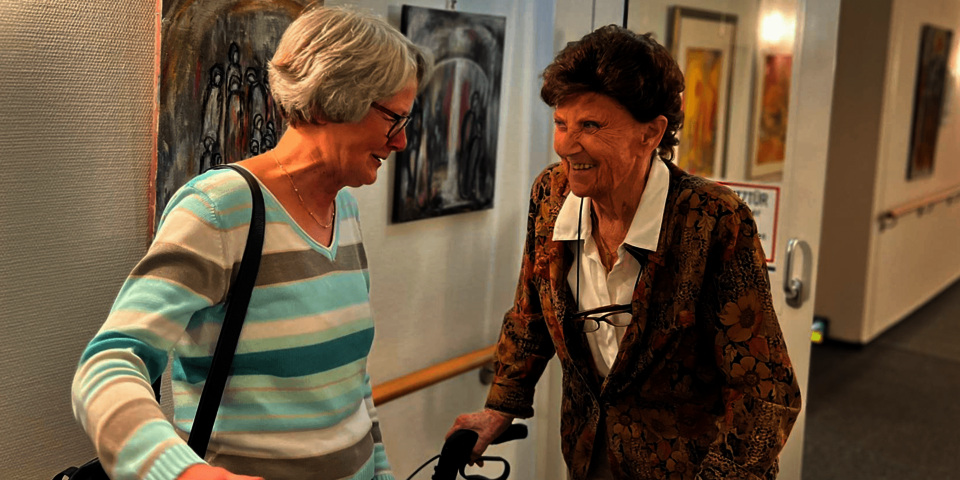 Zwei Frauen unterhalten sich in einem Flur vor Wandbildern.