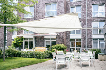 Blick auf die Fassade des Johanniter-Stiftes mit zahlreichen Sitzgelegenheiten unter einen Sonnensegel