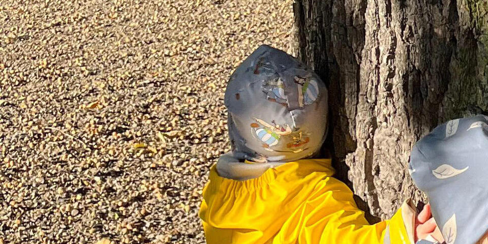 Ein Kind in gelber Jacke umarmt einen Baum