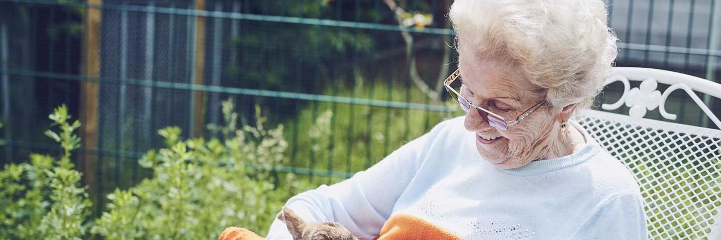 Eine Bewohnerin sitzt im Garten und streichelt Kaninchen