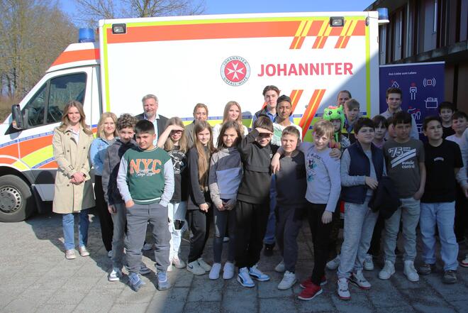Schüler stehen mit Rettungssanitätern und dem Personal der offenen Ganztagsschule vor dem Rettungswagen
