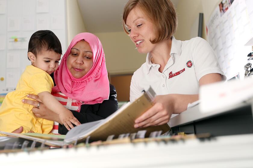 Zu sehen ist eine Mutter mit Kind, die Unterstützung bekommt beim Ausfüllen eines Formulars