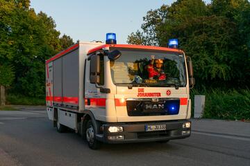 Ein Einsatzfahrzeug der Johanniter mit eingeschaltetem Blaulicht fährt auf einer Straße. Im Fahrerhaus sitzt eine Einsatzkraft in Uniform.