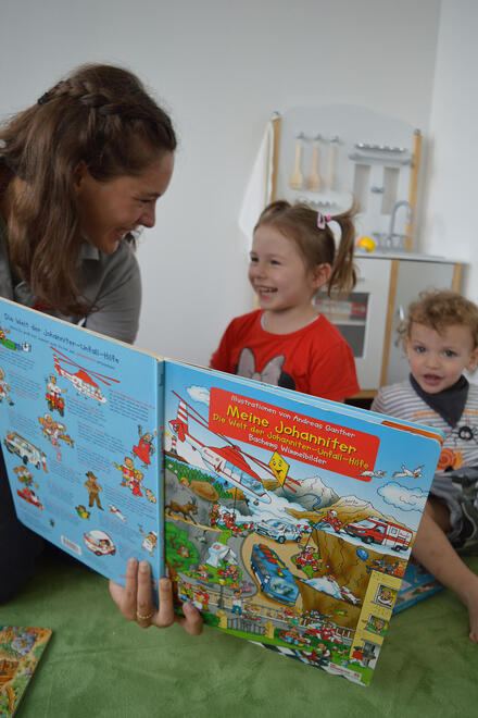 Eine Mitarbeiterin zeigt zwei Kindern ein Bilderbuch.