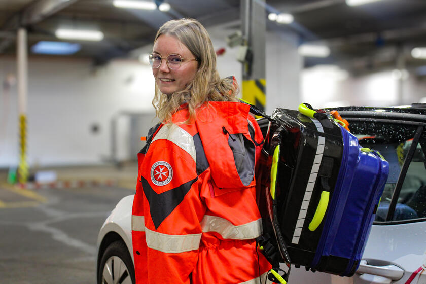 Eine junge Frau mit Johanniter-Bekleidung und einem Rettungsrucksack über der Schulter