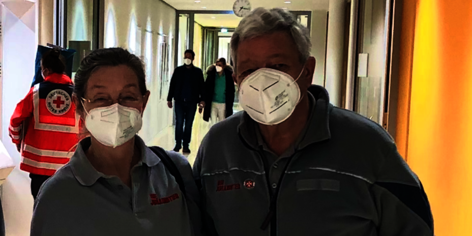 Zwei Johanniter-Helfer mit Masken stehen in einem Krankenhausflur.