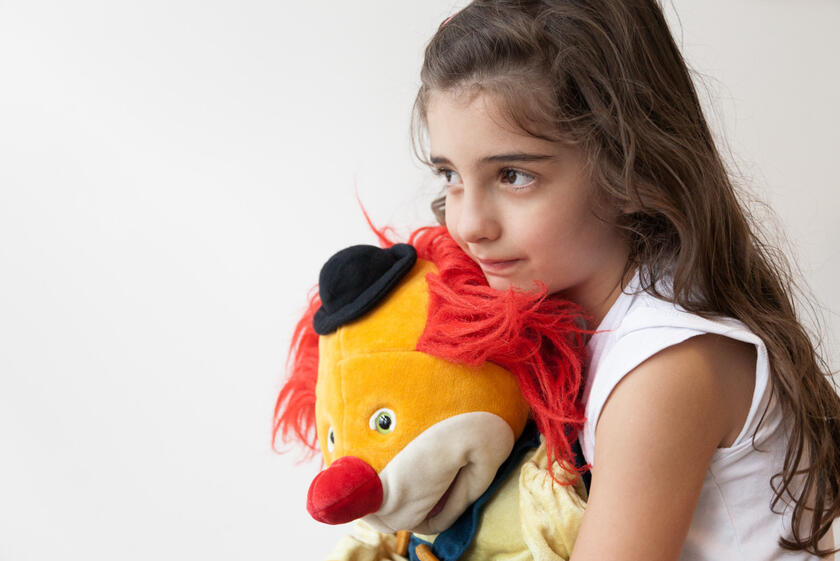 Kind umarmt Clown-Puppe – ein stiller Moment in der Trauerarbeit.