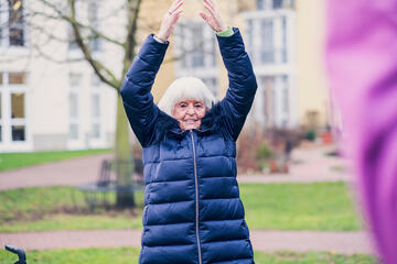 Eine Damen in einer blauen Jacke macht Sport in einer Gruppe