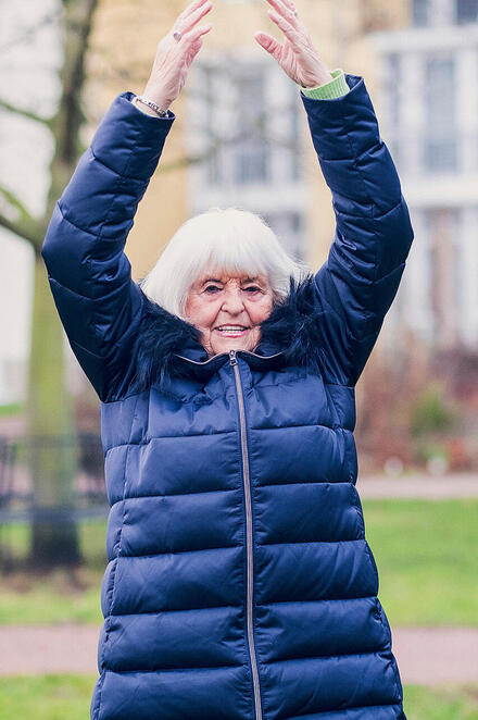 Eine Damen in einer blauen Jacke macht Sport in einer Gruppe