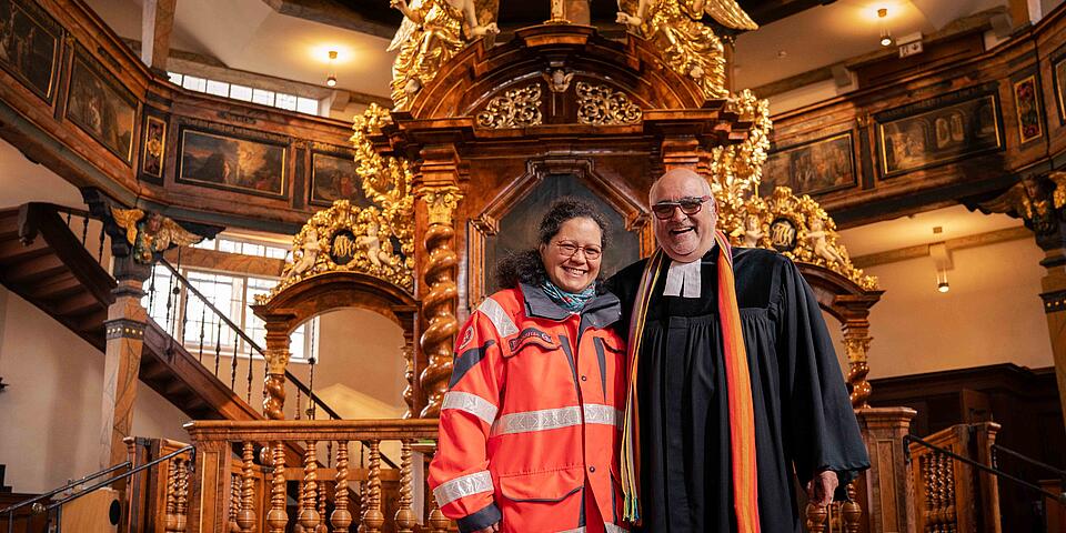 Zwei Menschen schauen in die Kamera beim Gottesdienst.