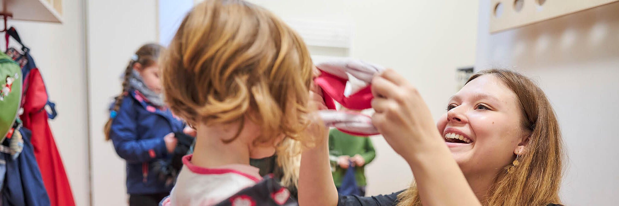 Eine Erzieherin hilft einem Kinder beim Anziehen.