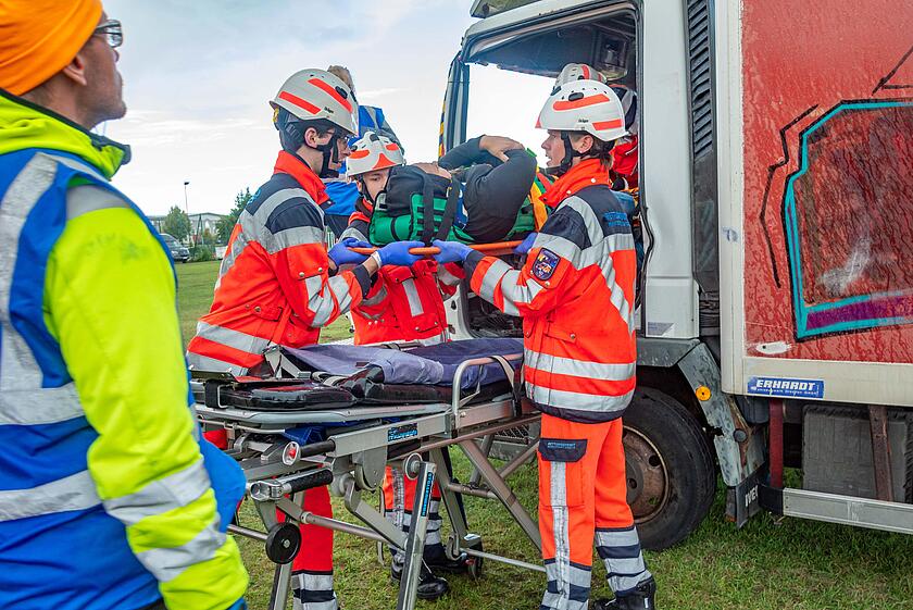 Mehrere Einsatzkräfte retten einen Darsteller auf einem Rettungsbrett aus einem Lkw.