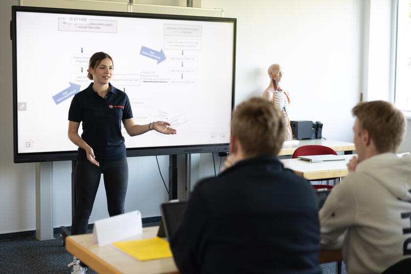 Dozentin der Johanniter erklärt Inhalte vor digitalem Whiteboard in einem Schulungsraum.