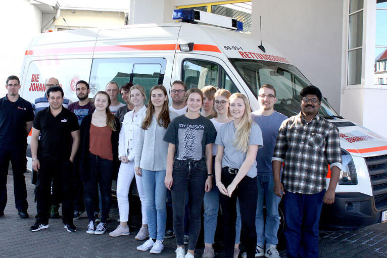 Gruppenbild der erfolgreichen Absolventenklasse vor einem Einsatzfahrzeug der Johanniter. 