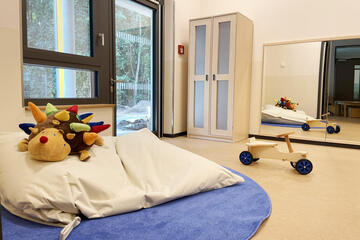 Ein heller Raum mit einem großem weichen Kissen und Kuscheltier sowie einem Tretauto.