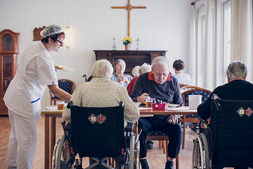 Eine Mitarbeiterin serviert den Bewohnenden die Speisen