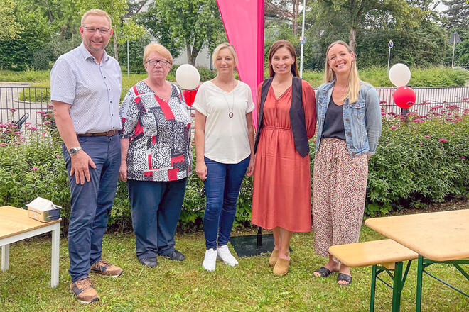 5 Leute stehen in einem Garten neben Bierbänken.