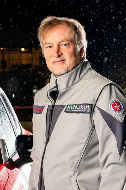 Ein Mann in einer Johanniter-Jacke vor einem Auto. Es ist dunkel
