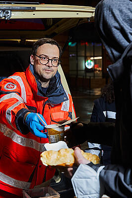 Ein Helfender des Kältebus gibt Essen an eine bedürftige Person aus