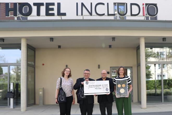 Vier Menschen stehen vor dem Hotel INCLUDiO und halten einen Spendenscheck in die Höhe