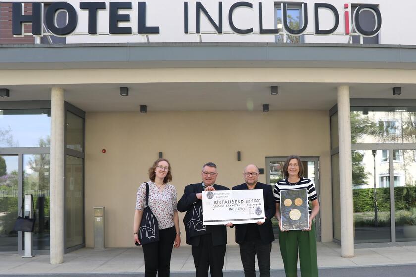 Vier Menschen stehen vor dem Hotel INCLUDiO und halten einen Spendenscheck in die Höhe
