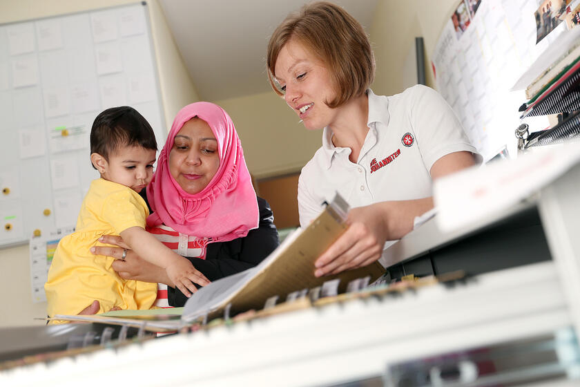 Mutter mit Kleinkind im beratenden Gespräch mit einer Johanniterin über Dokumente.