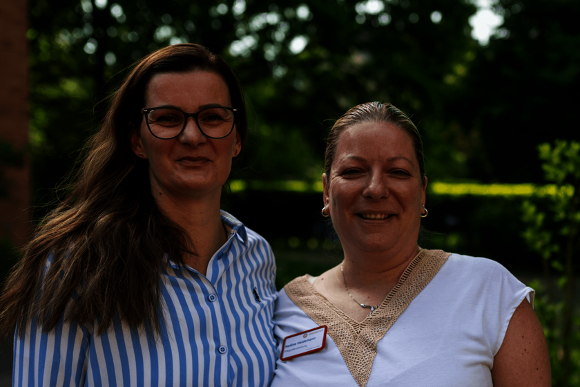 Zwei Frauen lächeln gemeinsam in einem Garten, Porträtaufnahme.  