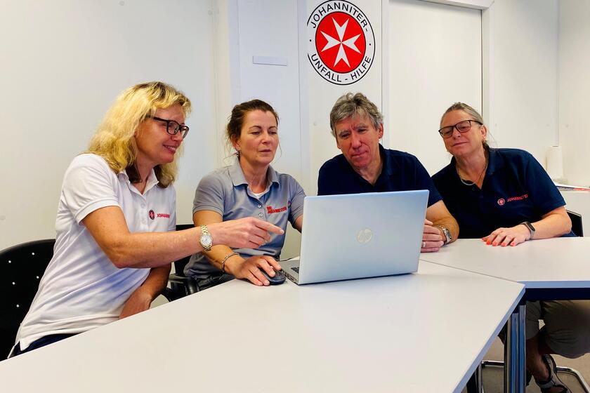 Vier Mitarbeiter der Antragsberatung besprechen eine Statistik auf einem Laptopbildschirm.