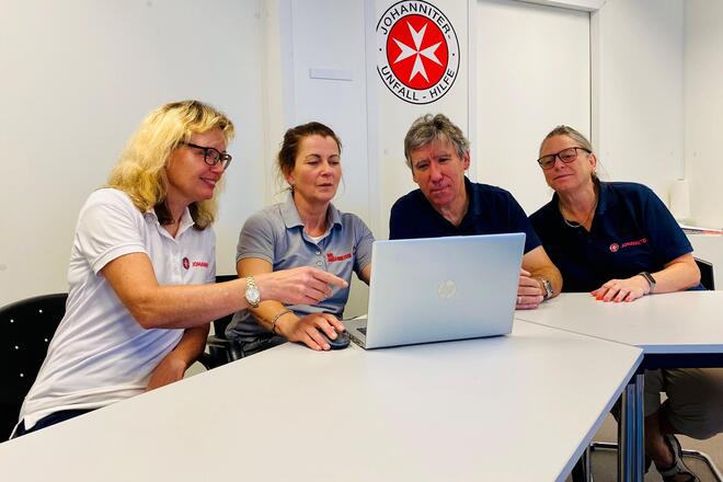 Vier Mitarbeiter der Antragsberatung besprechen eine Statistik auf einem Laptopbildschirm.