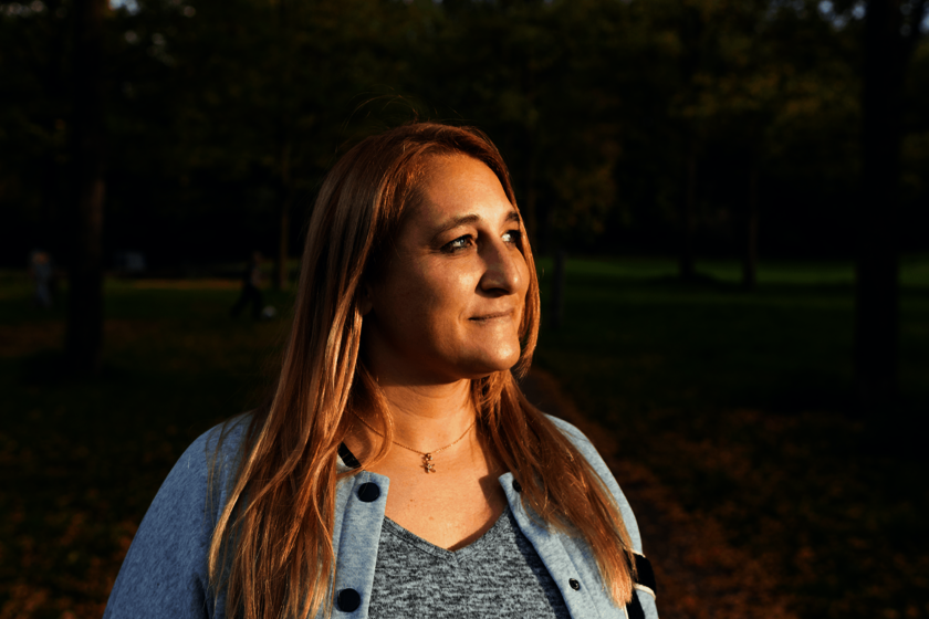 Eine Frau in einer Parkanlage. Sie hat lange rötliche-blonde Haare und blickt seitlich vom Fotografen weg. 