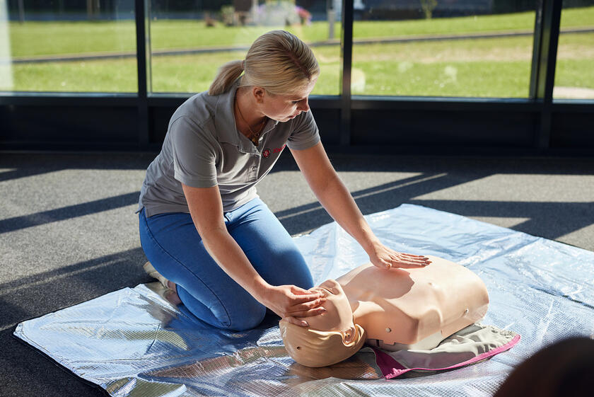 Frau übt Herz-Lungen-Wiederbelebung an Puppe bei Erste-Hilfe-Fortbildung.