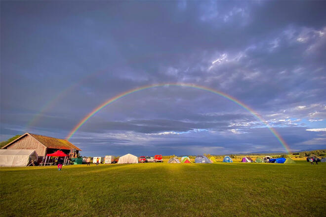 Ein Regenbogen erstreckt sich über eine große Grünfläche, auf der Zelte aufgeschlagen sind.