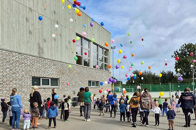 Kinder sowie Erzieherinnen und Erzieher lassen Ballons steigen.