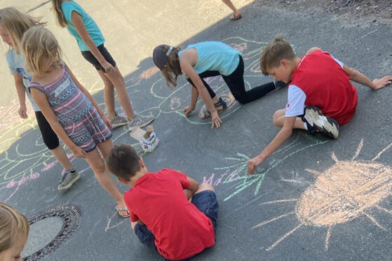 Kinder malen mit Kreide aus einen asphaltierten Weg 