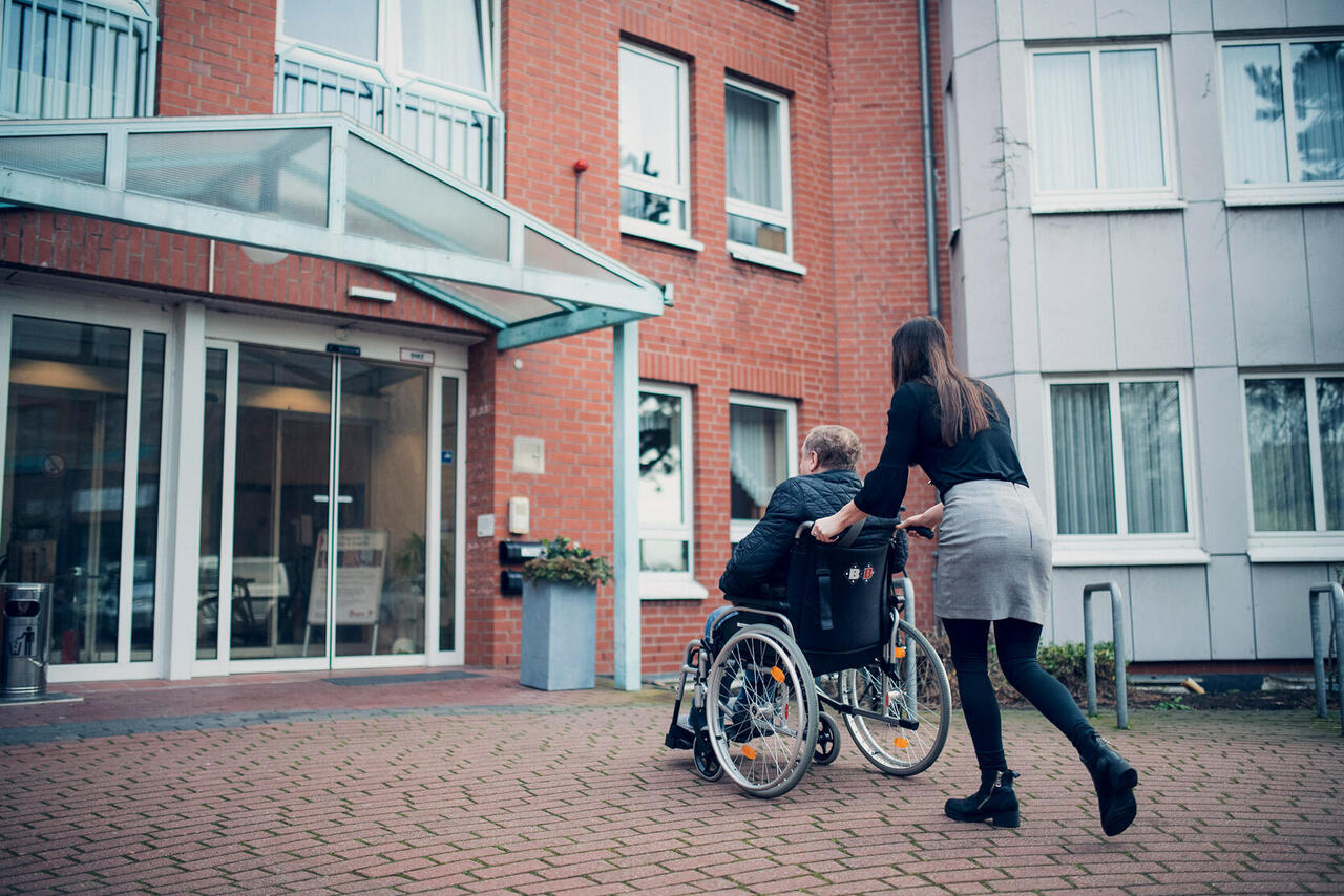 Eine junge Frau schiebt einen älteren Herren in das Johanniter-Haus Empelde