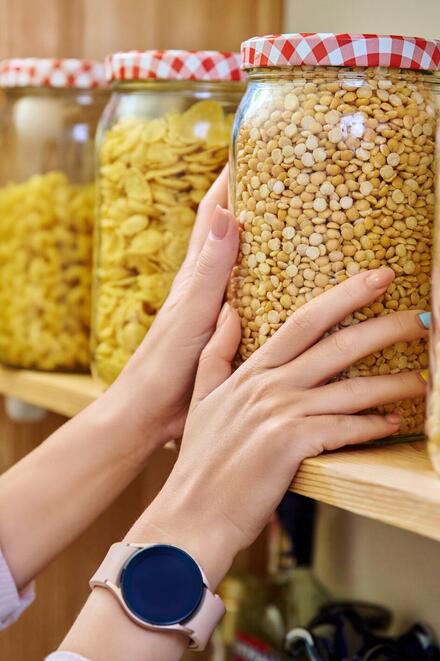 Eine Person greift mit beiden Händen nach einem Glas mit Vorräten im Regal.