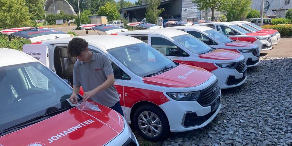11 neue, rot beklebte Fahrzeuge für den Johanniter-Hausnootruf-Einsatzdienst