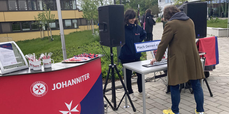 Eine Frau steht an einem Rollpiano. Eine Johanniterin steht bei ihr.