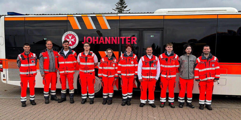 Zehn Frauen und Männer in Johanniter-Einsatzkleidung vor einem Johanniter-Bus
