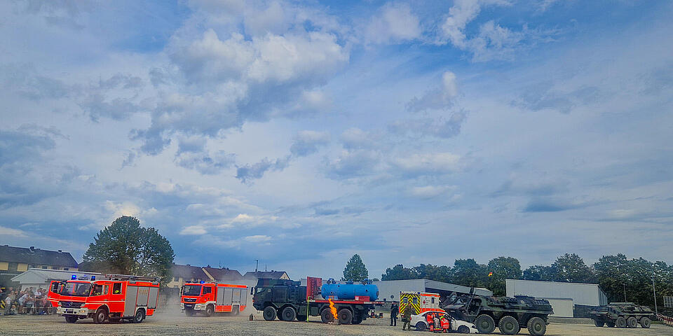 Auf einem Platz sind Feuerwehrfahrzeuge, ein weißer PKW, ein RTW, zwei Truppentransportpanzer und ein Militär-Gefahrgut-LKW zu sehen