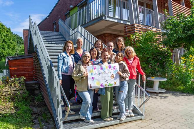 Die Mitarbeitenden der Johanniter-Kita stehen auf einer Treppe und halten ein Plakat hoch, auf dem steht: Stoppelhopser - das sind wir seit 10 Jahren.