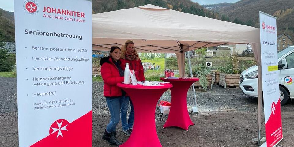 Zwei Mitarbeitende der Johanniter stehen am Stand der Infobustour der Johanniter-Fluthilfe