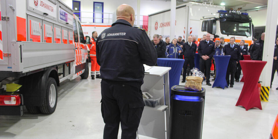   Mann in Johanniter-Kleidung spricht an einem Rednerpult vor Publikum in Einsatzkleidung. 