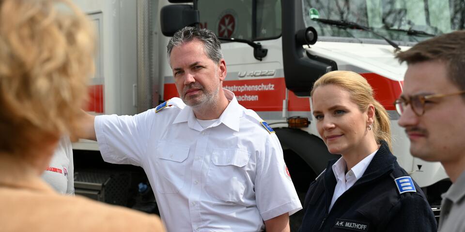 Zwei Männer und eine Frau in Johanniter-Bekleidung hören einer anderen Frau zu