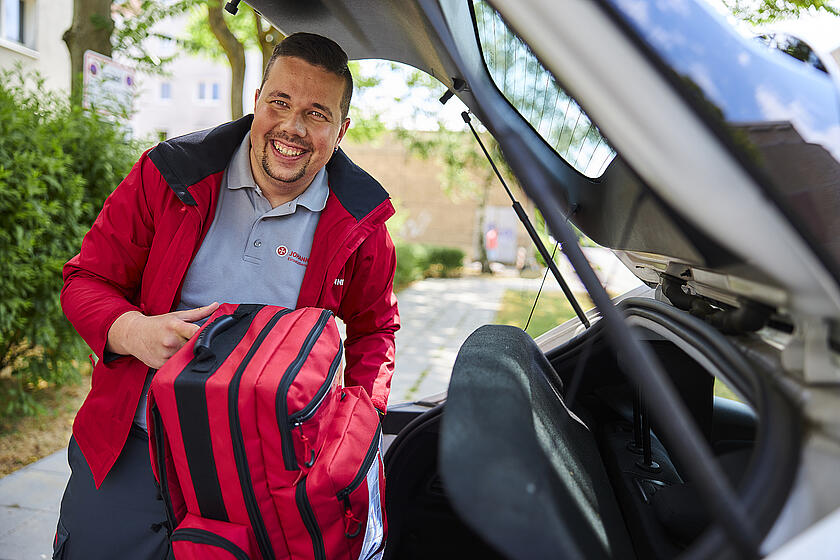 ein Mann mit dunklen Haaren in roter Einsatzjacke nimmt einen roten Rettungsrucksack aus einem Kofferraum