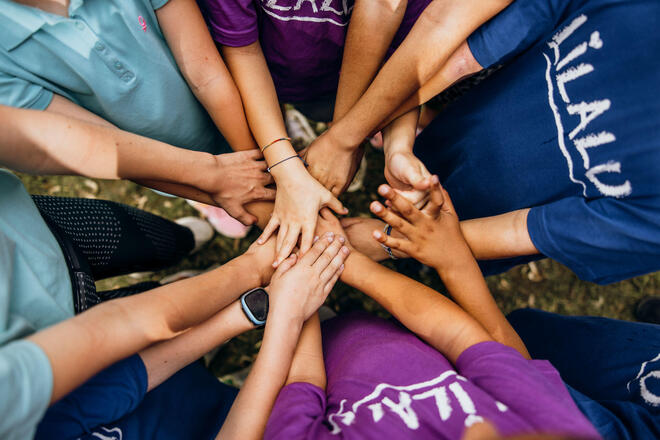 Kinder legen im Kreis ihre Hände übereinander als Zeichen für Teamgeist.