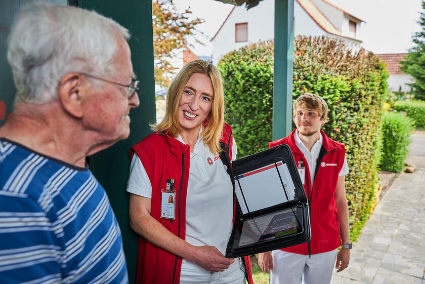 Johanniter Förderservice im freundlichen Gespräch mit älterem Herren an der Haustür.
