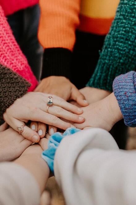 Mehrere Hände von Menschen in bunten Pullovern liegen übereinander und symbolisieren Zusammenhalt und Teamgeist.