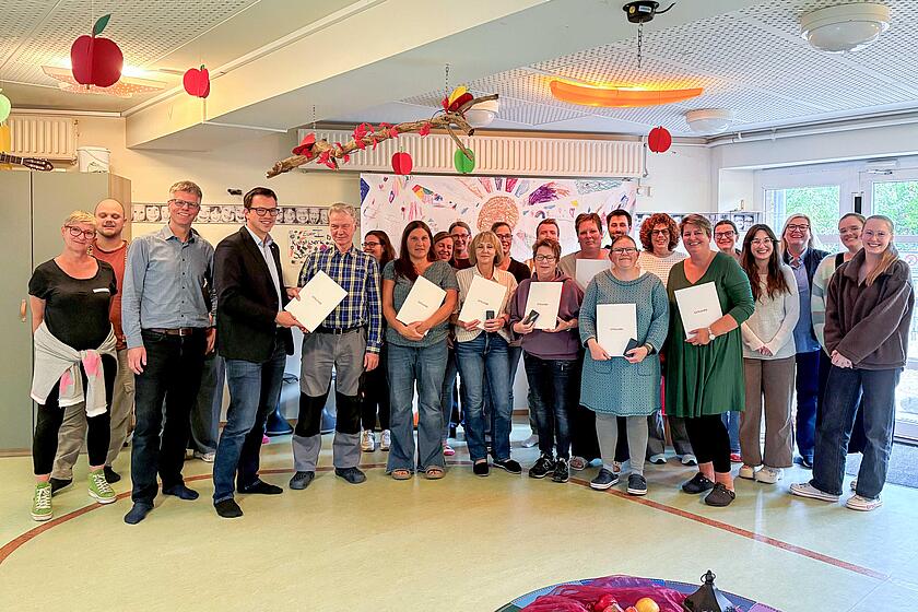 Yonathan Arnold, Mitglied im Regionalvorstand bei den Johannitern, übergibt Ingo Mischke die Ehrenurkunde für sein 25-jähriges Jubiläum. Acht weitere Mitarbeitende stehen dabei.