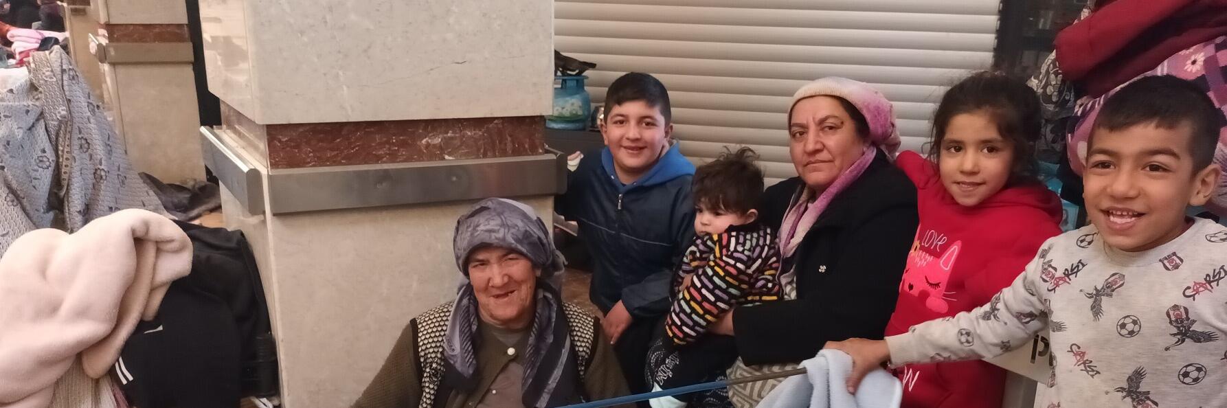 Zwei Frauen mit Kopftuch sitzen mit mehreren Kindern in einer Notunterkunft.